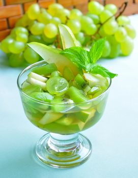 Fruit salad with grapes, kiwi, pears, topped with wine in the glass, decorated with mint leaves.

