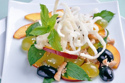 light salad with chicken, grapes, nectarines, sesame, with lemon dressing, decorated with fried rice noodles with mint