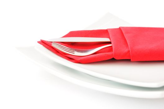 knife and fork in a red napkin on a white double square plate on a white background