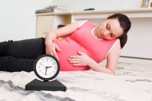 pregnant lying woman and clock, focus on clock