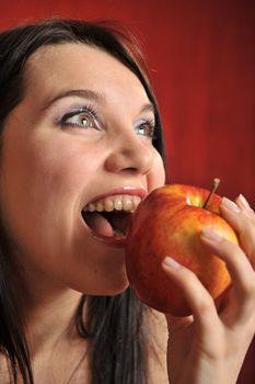 A portrait of a girl biting a red apple excitingly