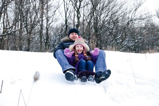 father and daughter riding on a sled in a winter woods