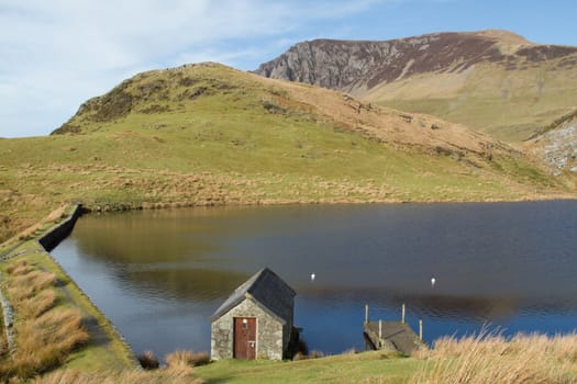 A stone boathouse with jetty on a dammed lake in the mountains with blue sky and cloud.