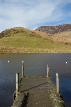 A small jetty landing site made of concrete with wooden posts on a lake in the mountains