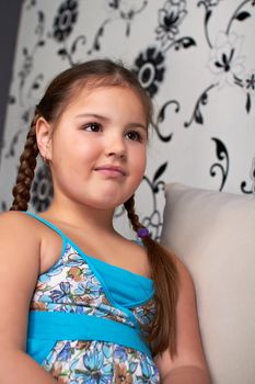 A little girl sits pensively on the couch.