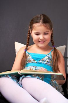 A little girl reads the book interesting and fascinating, lying on the couch.