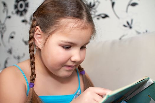 A little girl reads the book interesting and fascinating, lying on the couch.