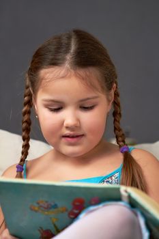 A little girl reads the book interesting and fascinating, lying on the couch.