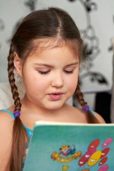 A little girl reads the book interesting and fascinating, lying on the couch.