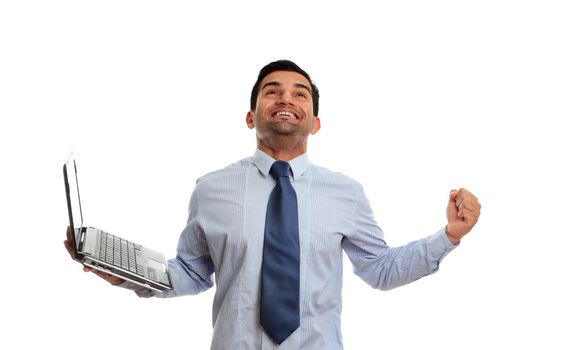 An excited man holding a laptop and raising arm in clenched fist and looking upward celebrates victory, achievement or success.