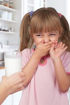 Cute little girl and glass of milk in kitchen