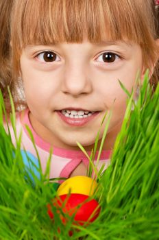 Little girl finds a multicoloured easter eggs in the tall green grass