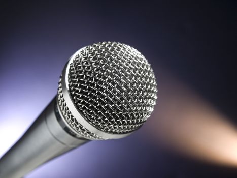 A dynamic microphone on stage. Color spot lights as background.