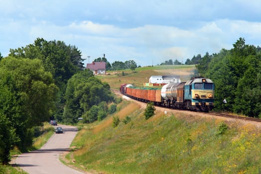Rural summer landscape with freight train hauled by the diesel locomotive running through the countryside
