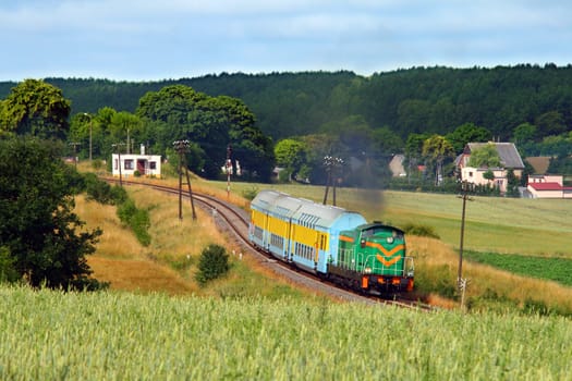 Rural summer landscape with train hauled by the diesel locomotive running through the countryside