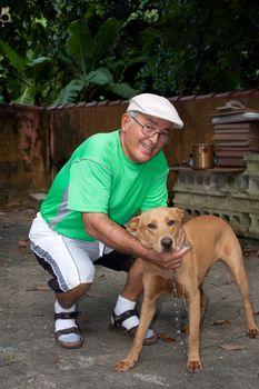 An elderly Hispanic senior citizen man petting his dog with a large smile on his face.