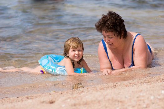 Grandmother and grandchild having fun in the water on the beach hot sunny day
