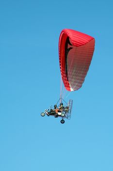 trike dual paragliding on red wing, clear blue sky