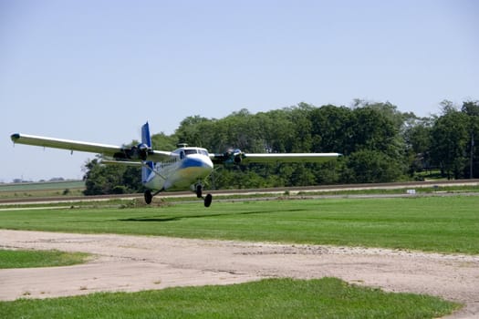 This is a medium sized twin engine propeller airplane landing on a grass landing strip.