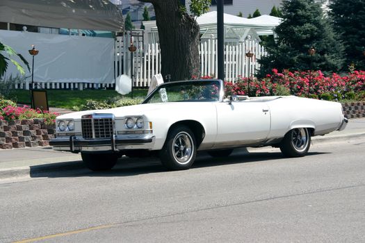 This is a picture of a white 1970's convertible on a street taken on a sunny day with the top down.
