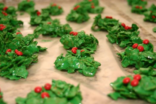 These are Christmas cookies that are made with marshmallows melted in butter, green food dye and breakfast flakes with red cinnamon candies on top spread out on wax paper.