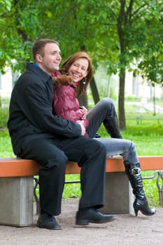 Happy young couple sitting on bench in park