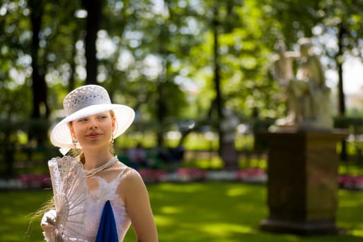 Young lady wearing white hat holding fan walking in park 