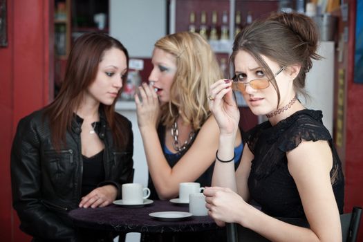 Two friends share a secret while a woman looks away with eyeglasses down