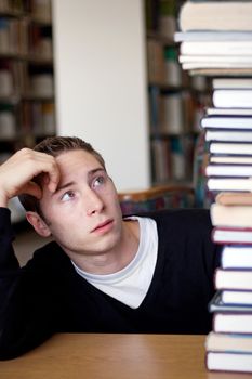 A frustrated and stressed out student looks up at the high pile of textbooks he has to go through to do his homework.