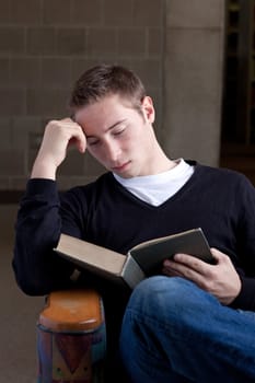 A young college aged man reading a book at the library.