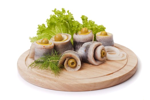 A composition with marinated herring rolls and vegetables on wooden plate isolated on white