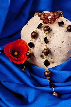 Necklace, flower and stone on a blue textile. Vertical