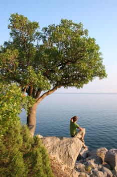 Man sitting on the rock under the tree and looking into horizon