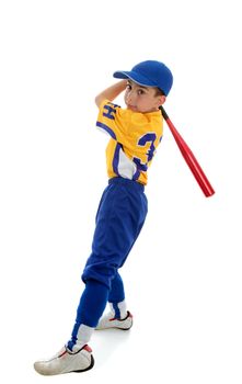 A young boy in a softball, baseball or t-ball uniform swings a bat.  White background.