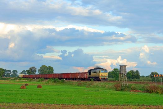 Freight train hauled by the diesel locomotive is passing the countryside