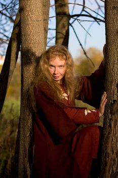 The blonde girl in medieval red dress in the autumn forest
