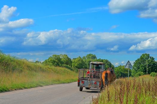 Tractor with trailor and two horses riding the road with the colorful sky over