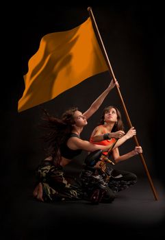Two young girl rising flag with paintball gun in their hands. File includes clipping path of flag.