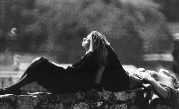 Black and white photo of two young girls sitting and resting on stone wall.