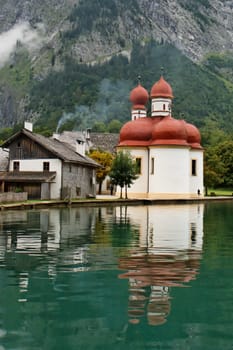 Red domes of St. Batholomä Church reflect in the green lake water