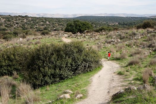 Lonely little boy walks along the trail among hills outdoor