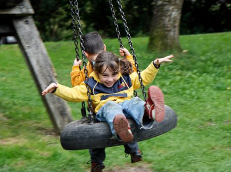 Little girl and boy swing on a hanging tire