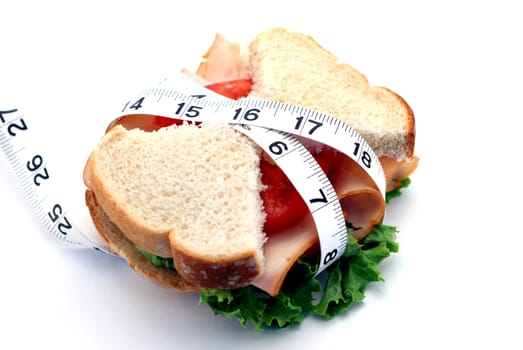 Low-carb diet concept with a turkey sandwich, skinny bread, and tape measure over a white background