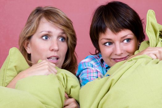 Two girl watching a scary movie while hugging their pillows for comfort