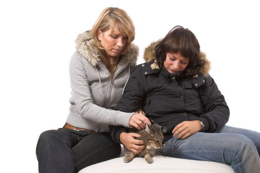 Two girl stroking the cat who looks a bit unwilling 