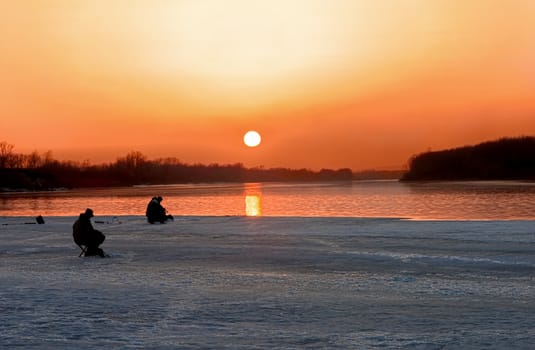 Two fishermen fish in the evening on a sunset