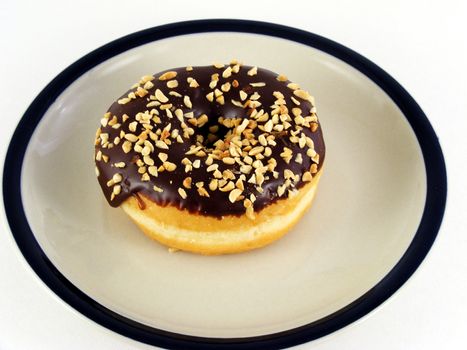 A chocolate iced donut with nuts on a plate against a white background.