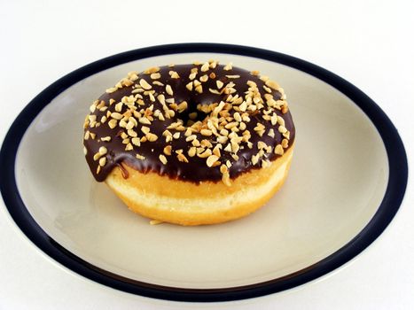 A chocolate iced donut with nuts on a plate against a white background.