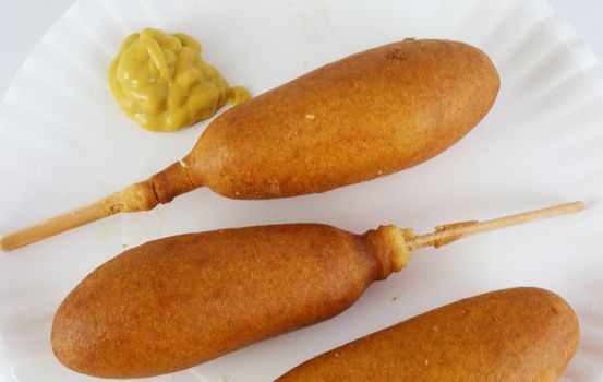 Three corn dogs and mustard on a paper plate.