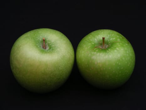 A pair of granny smith apples against a black background.